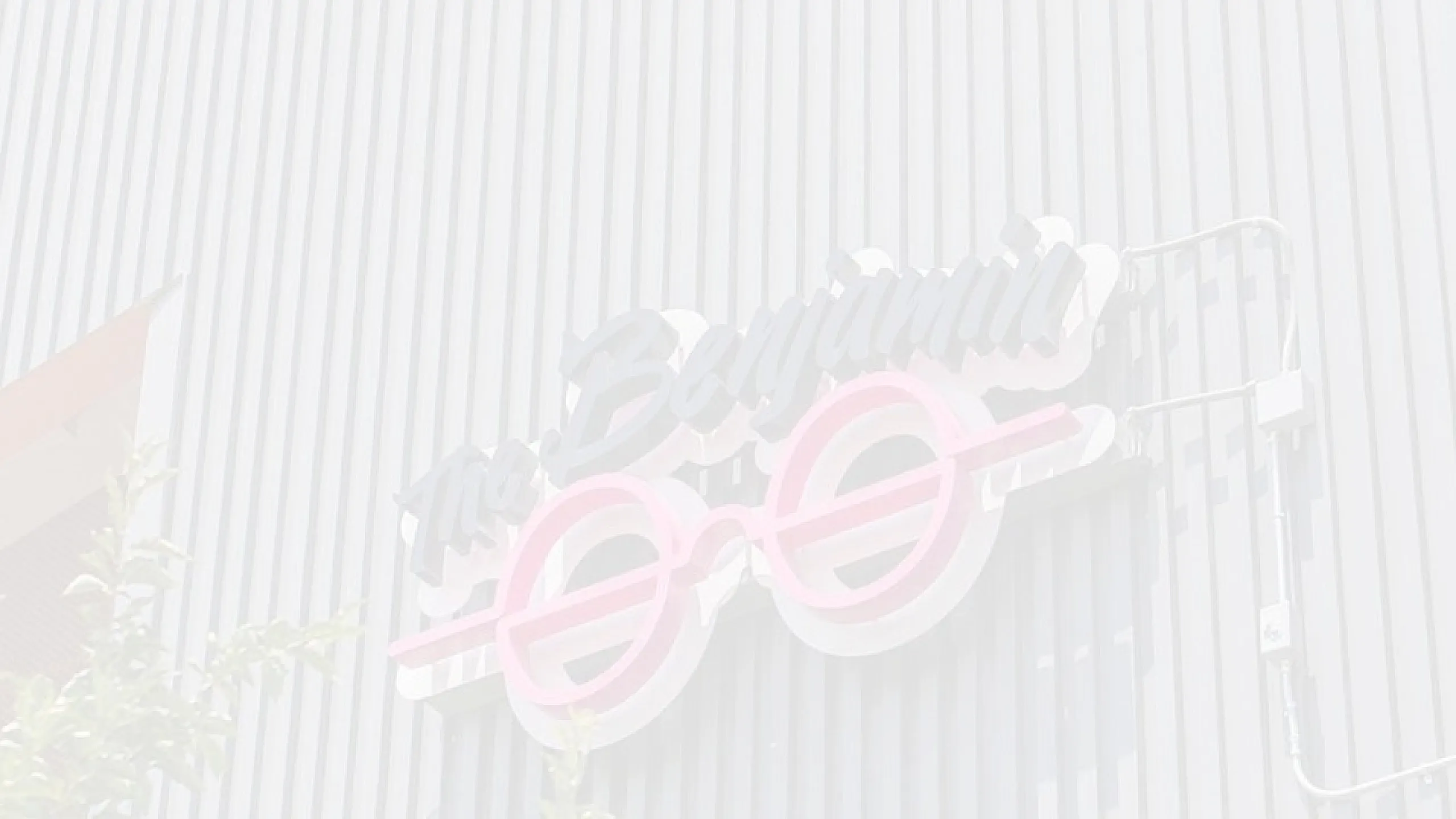 Modern building facade featuring stylish ribbed metal siding and vibrant neon glasses sign.
