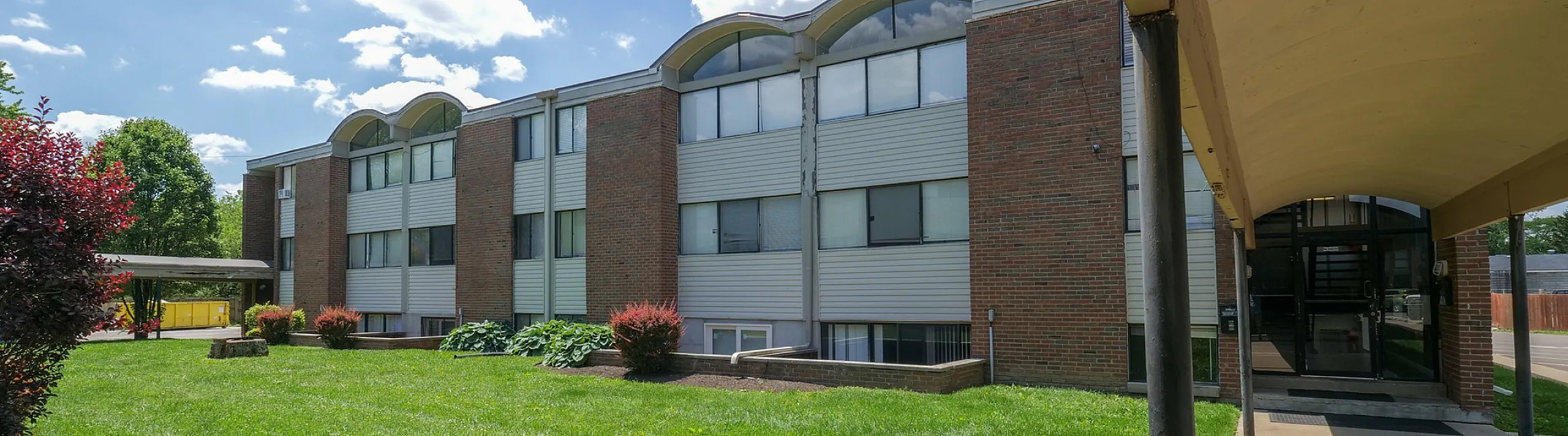 Elegant apartment building with modern brick facade, nestled in lush green surroundings under a clear blue sky.