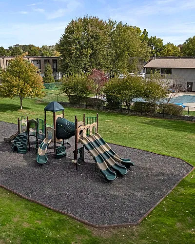 Charming apartment complex with a vibrant playground and tennis court, set amidst lush greenery.
