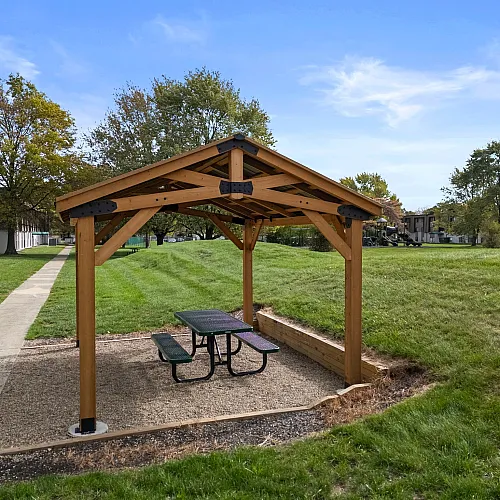 Charming outdoor picnic area with a wooden gazebo and lush green surroundings, perfect for relaxation and enjoyment.