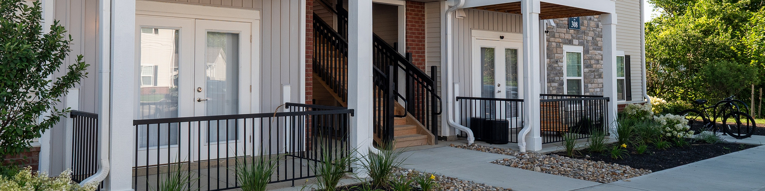 Charming apartment entrance with modern balconies, lush landscaping, and elegant exterior design.