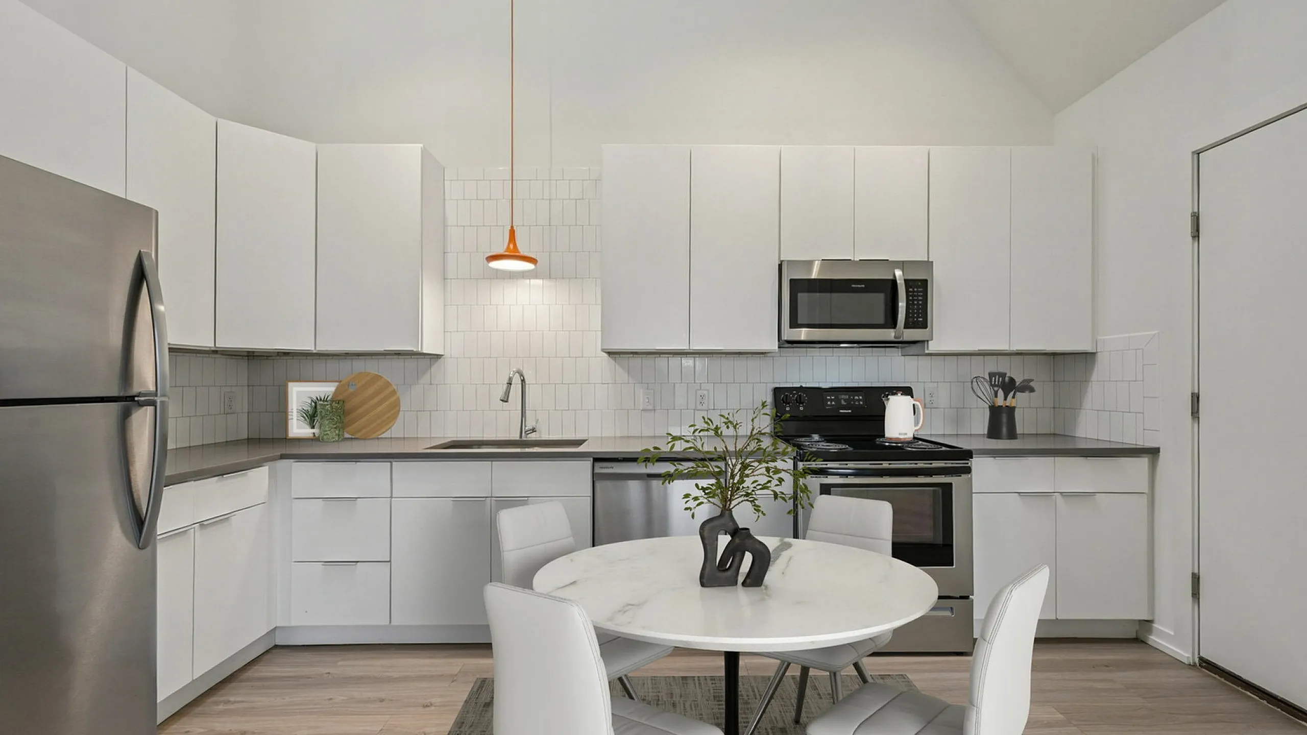 Sleek modern kitchen with white cabinetry, stainless steel appliances, and a cozy round dining table under a stylish pendant light.