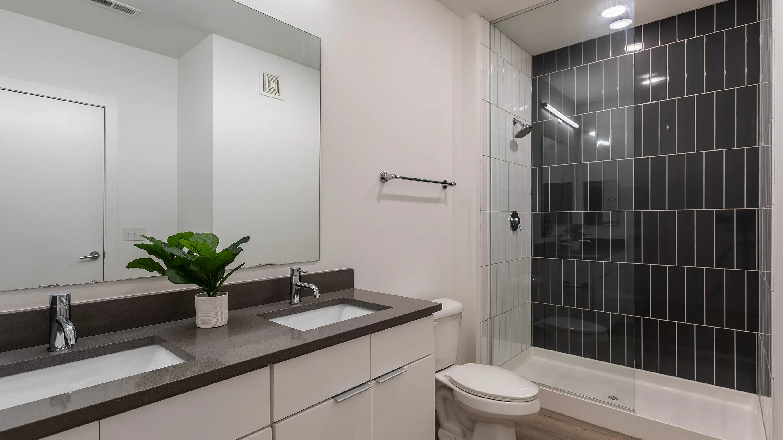 Elegant, modern bathroom featuring double sinks, sleek glass-enclosed shower, and stylish dark tile accents.