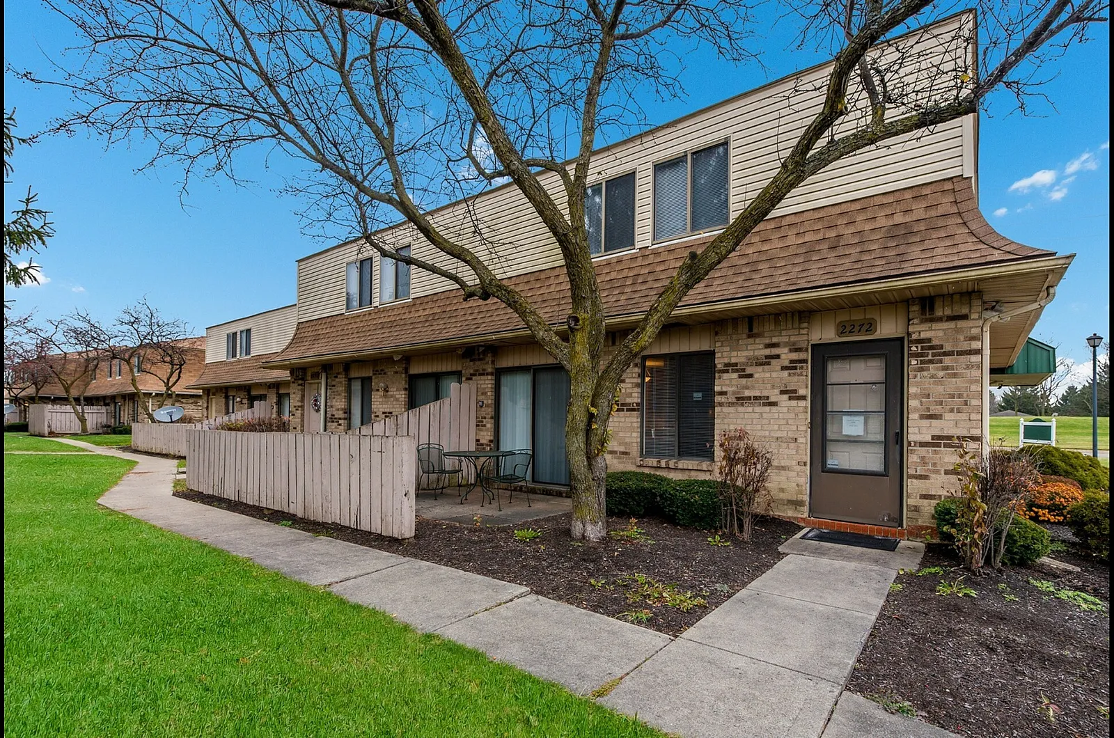 Inviting townhome with charming brick exterior, private patio, and lush green surroundings, perfect for a serene lifestyle.