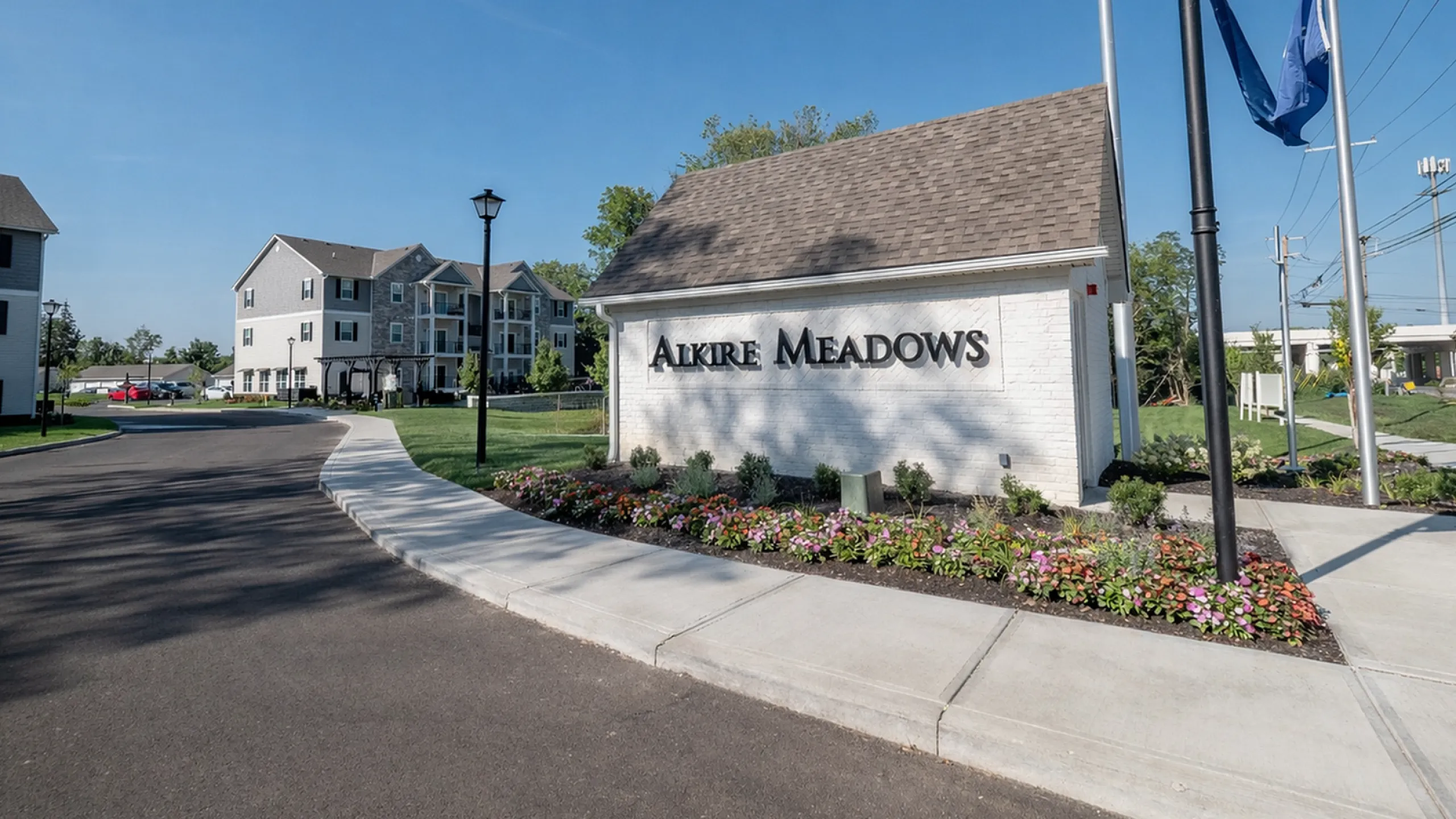 Inviting entrance to Alkire Meadows with beautiful landscaping and modern apartment buildings in the background.