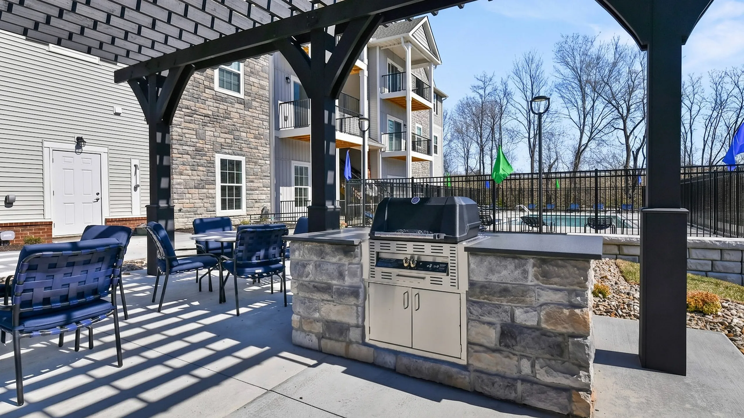 Inviting outdoor space with a stylish grill area under a charming pergola, perfect for gatherings, adjacent to a modern apartment building.