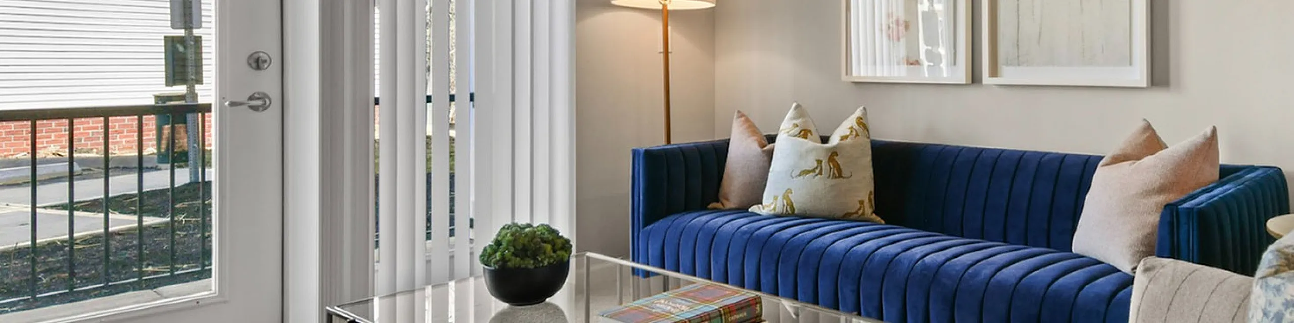 Bright and cozy living room with a modern blue sofa, elegant glass coffee table, chic wall art, and large windows offering abundant natural light.