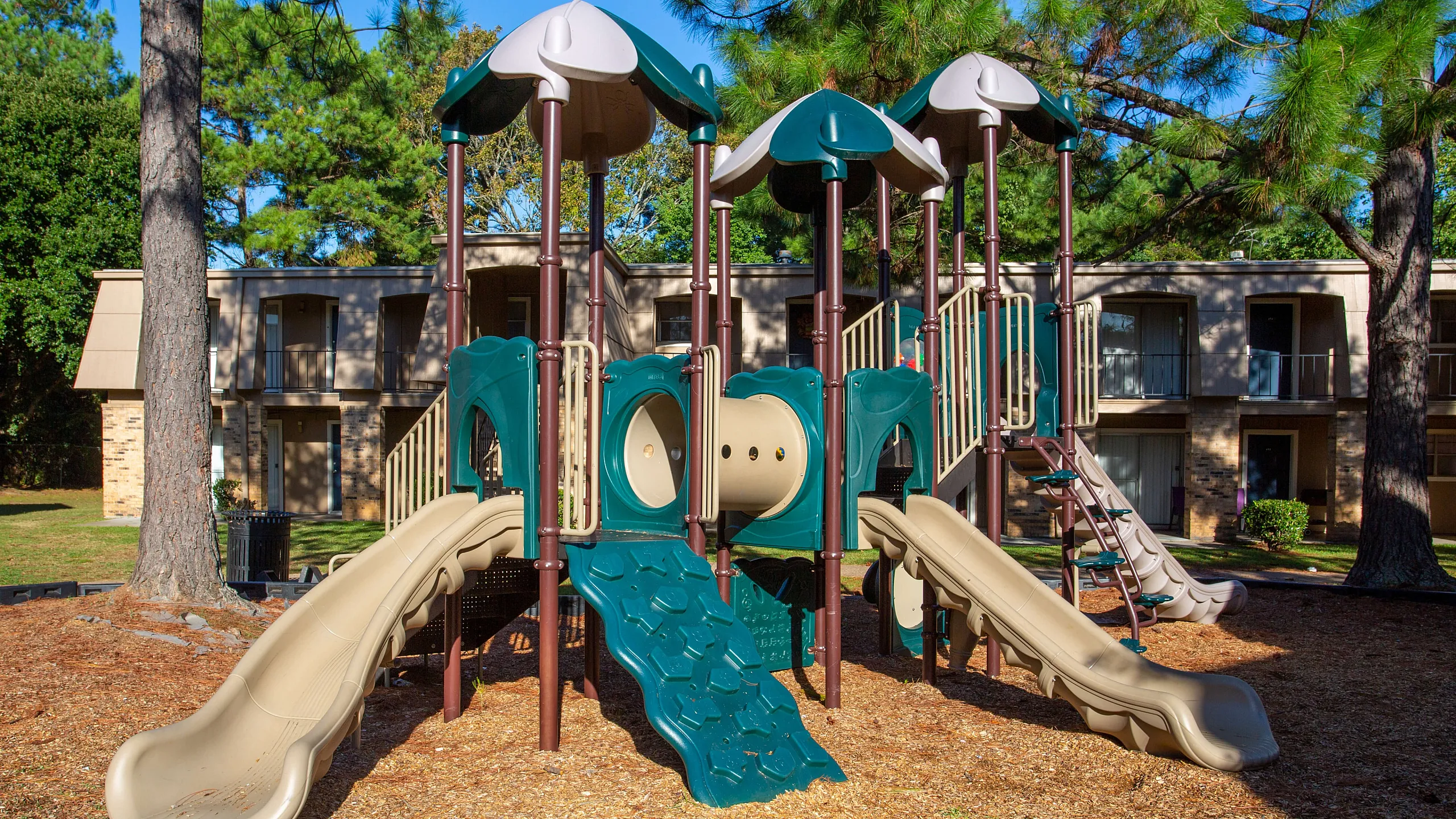Charming residential playground surrounded by lush greenery, featuring multiple slides and climbing elements for endless family fun.