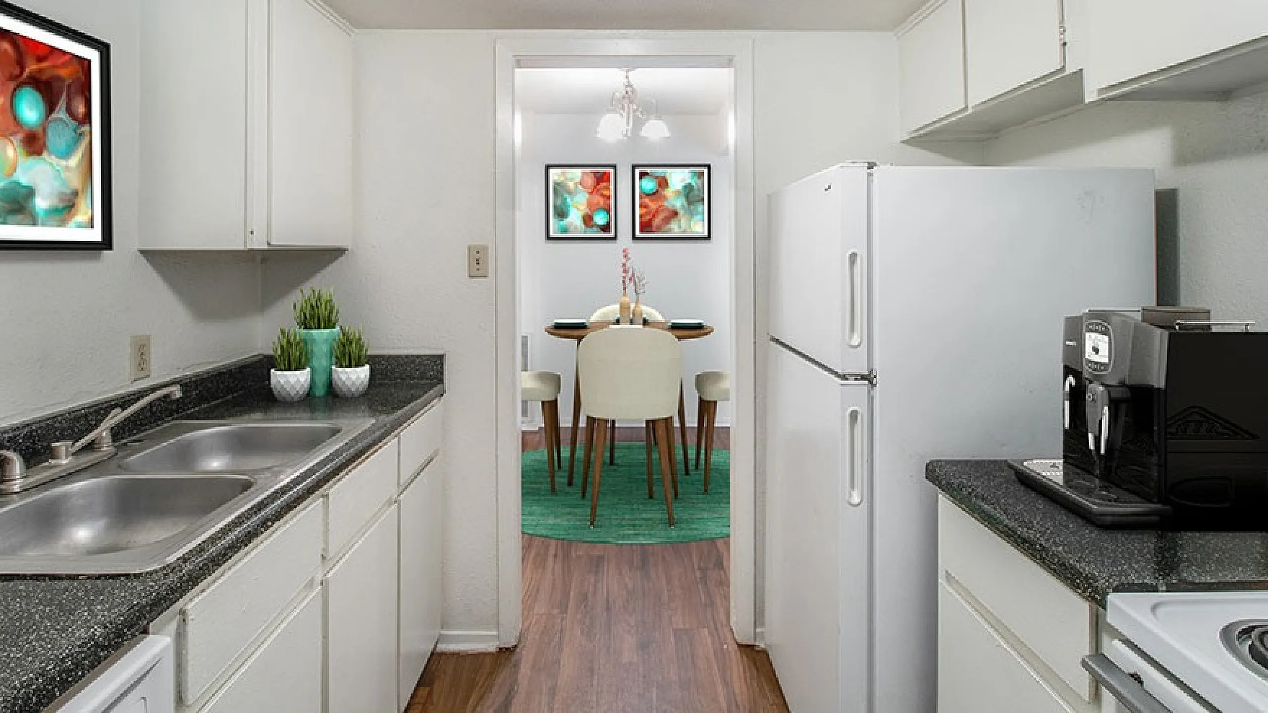 Modern kitchen with sleek countertops, stainless steel sink, and dining area view, featuring artistic decor and lush greenery.