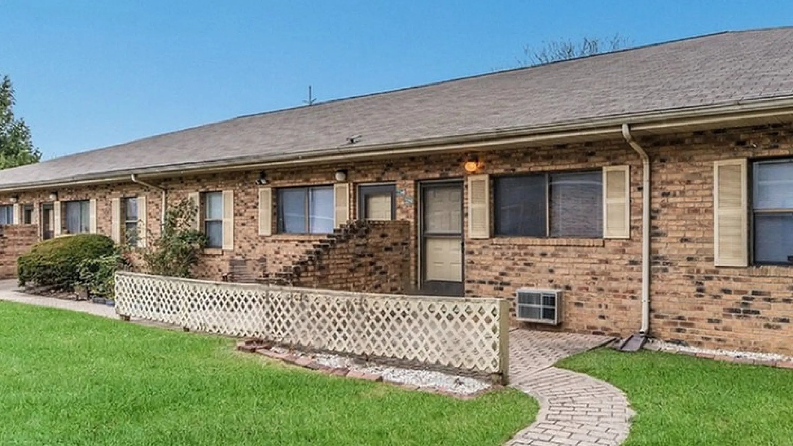 Charming brick apartment building with manicured lawns and a welcoming pathway entrance.