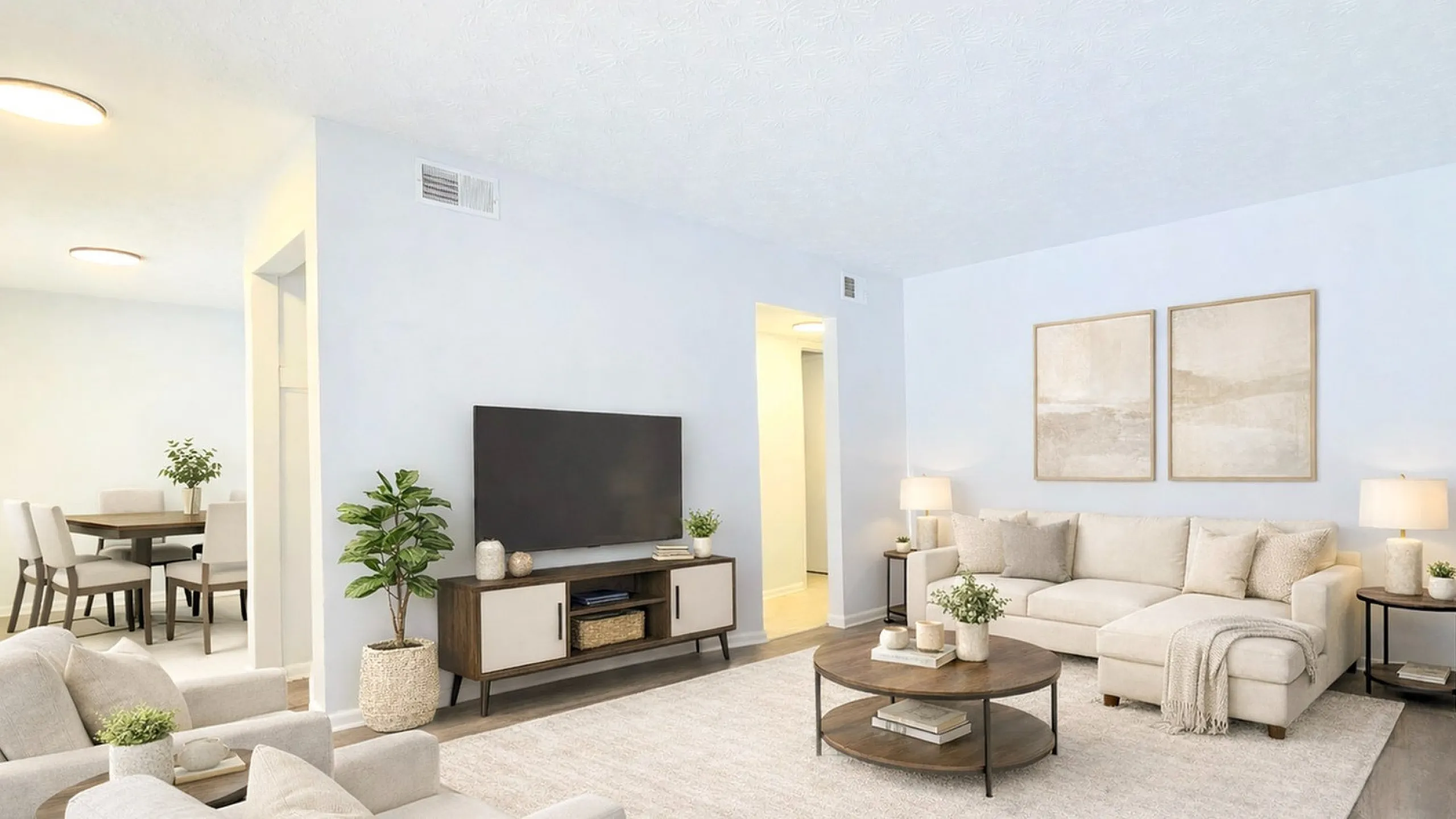Bright and inviting living room featuring a modern white sectional sofa, stylish coffee table, and elegant decor. The open-concept space seamlessly connects to a cozy dining area with chic seating, perfect for effortless entertaining.