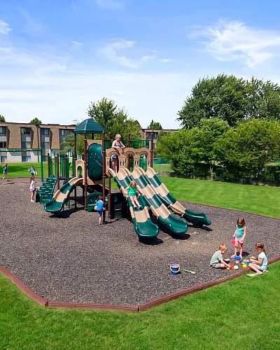 Lush apartment complex playground featuring vibrant slides, swings, and children enjoying open green spaces on a sunny day.