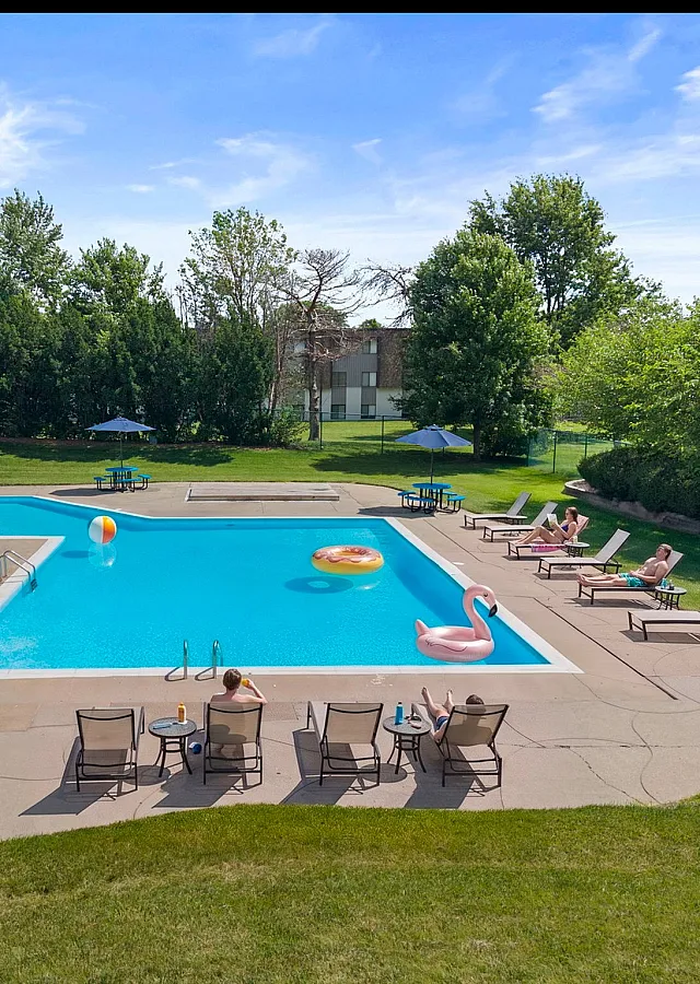 Inviting outdoor pool area with lounge chairs, umbrellas, and vibrant floats set amidst lush greenery, ideal for relaxation and summer enjoyment.