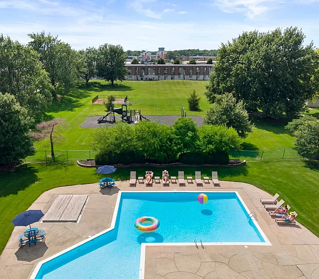 Lush green landscape with a sparkling outdoor pool, surrounded by lounge chairs and umbrellas, perfect for relaxation and enjoying sunny days.