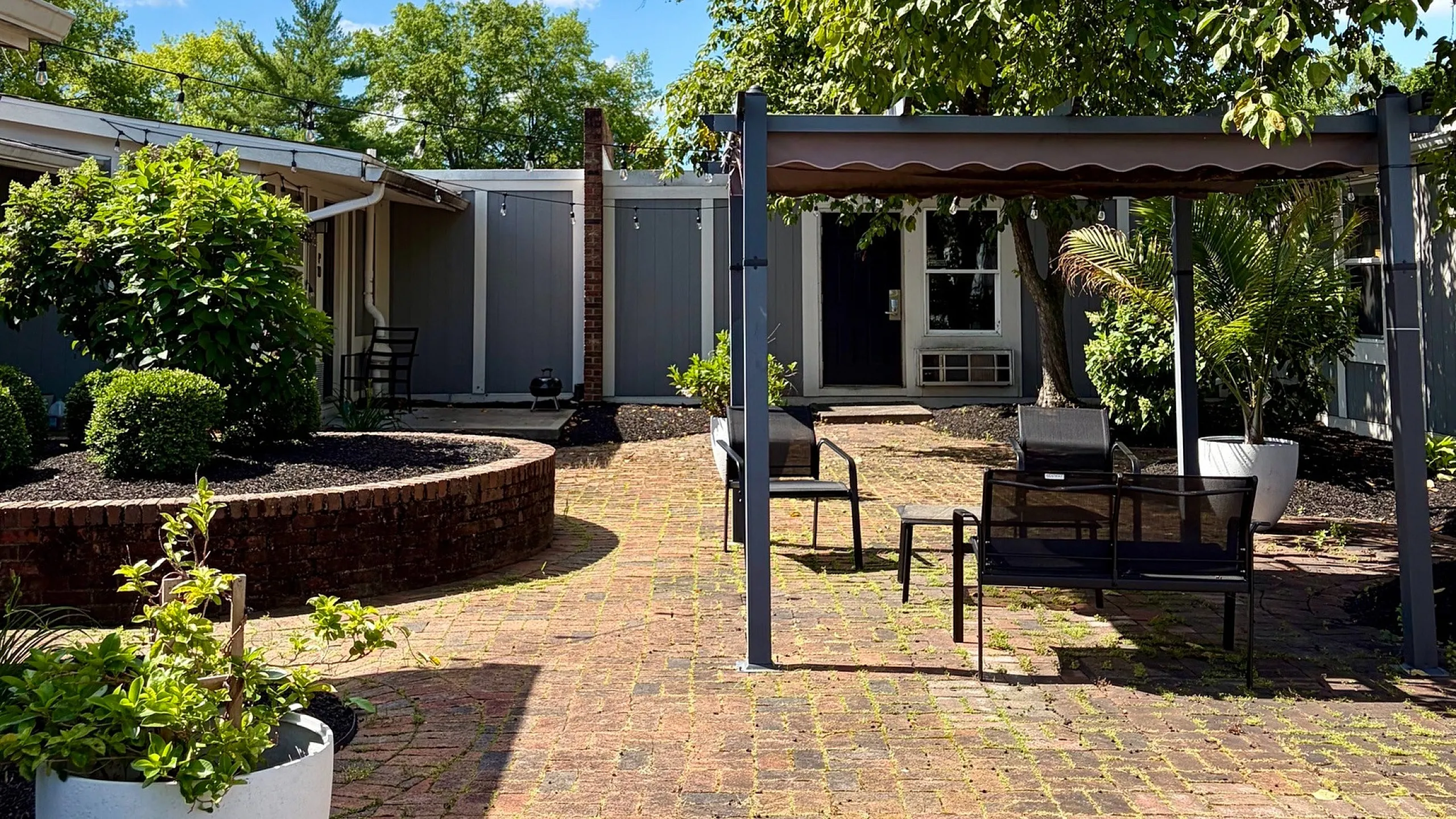 Charming brick patio with inviting outdoor seating under lush greenery on a sunny day.