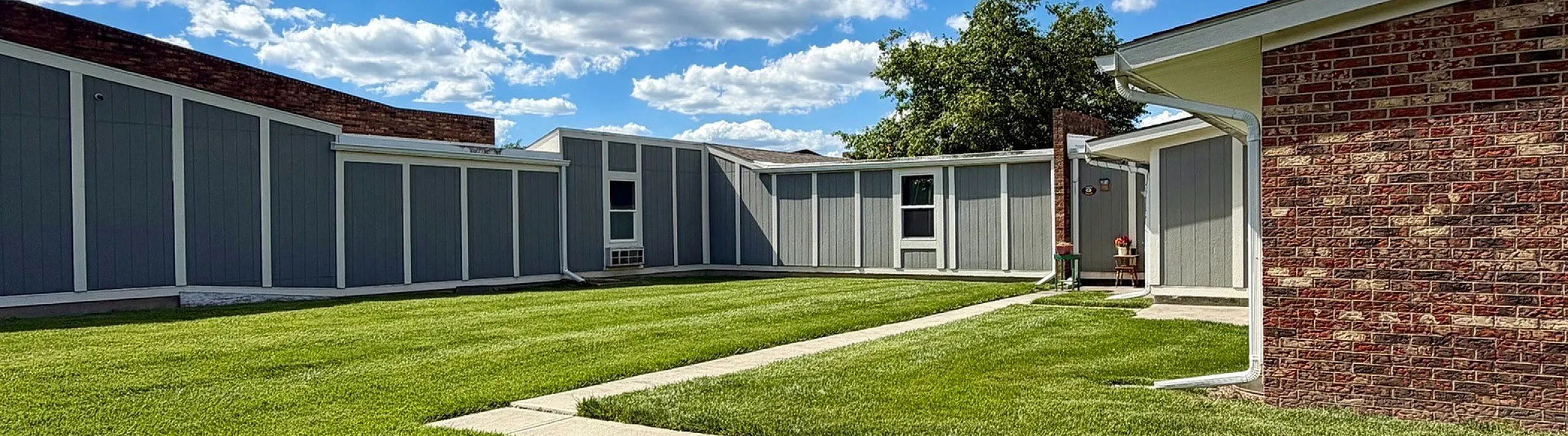 Charming courtyard with lush green lawn and bright blue sky, offering a serene outdoor escape in a quiet residential area.