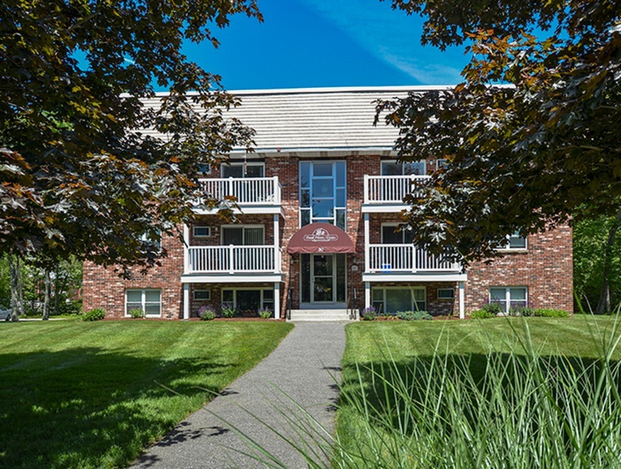 Exterior of a brick building with 4 balconies and 2 patios, trees and green grass.