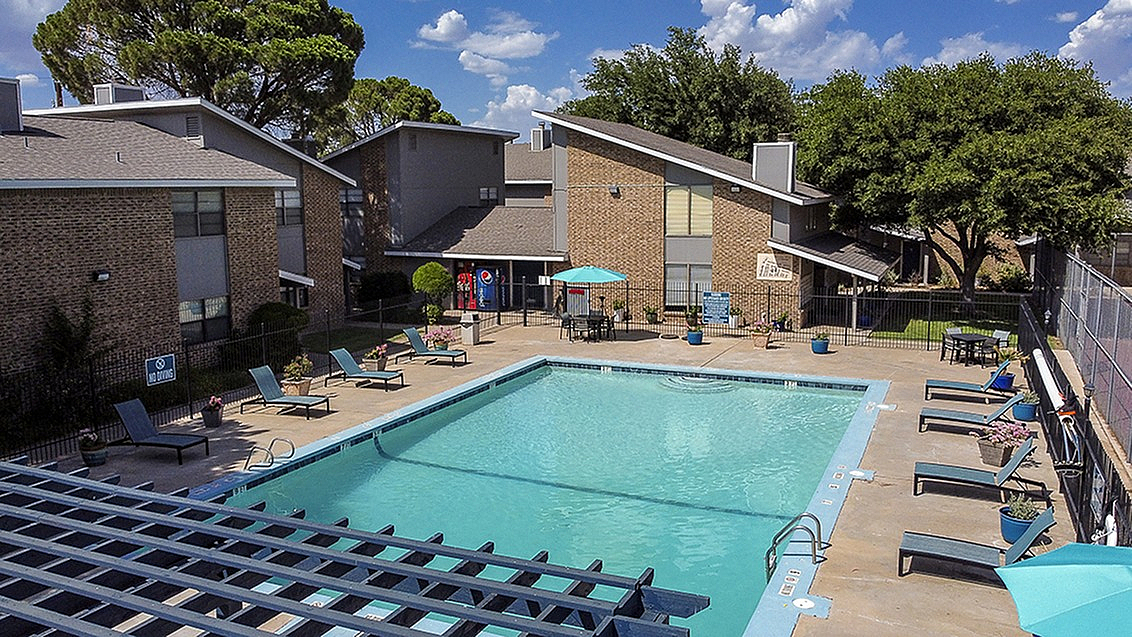 Charming apartment complex with a spacious swimming pool surrounded by lounge chairs and vibrant greenery.