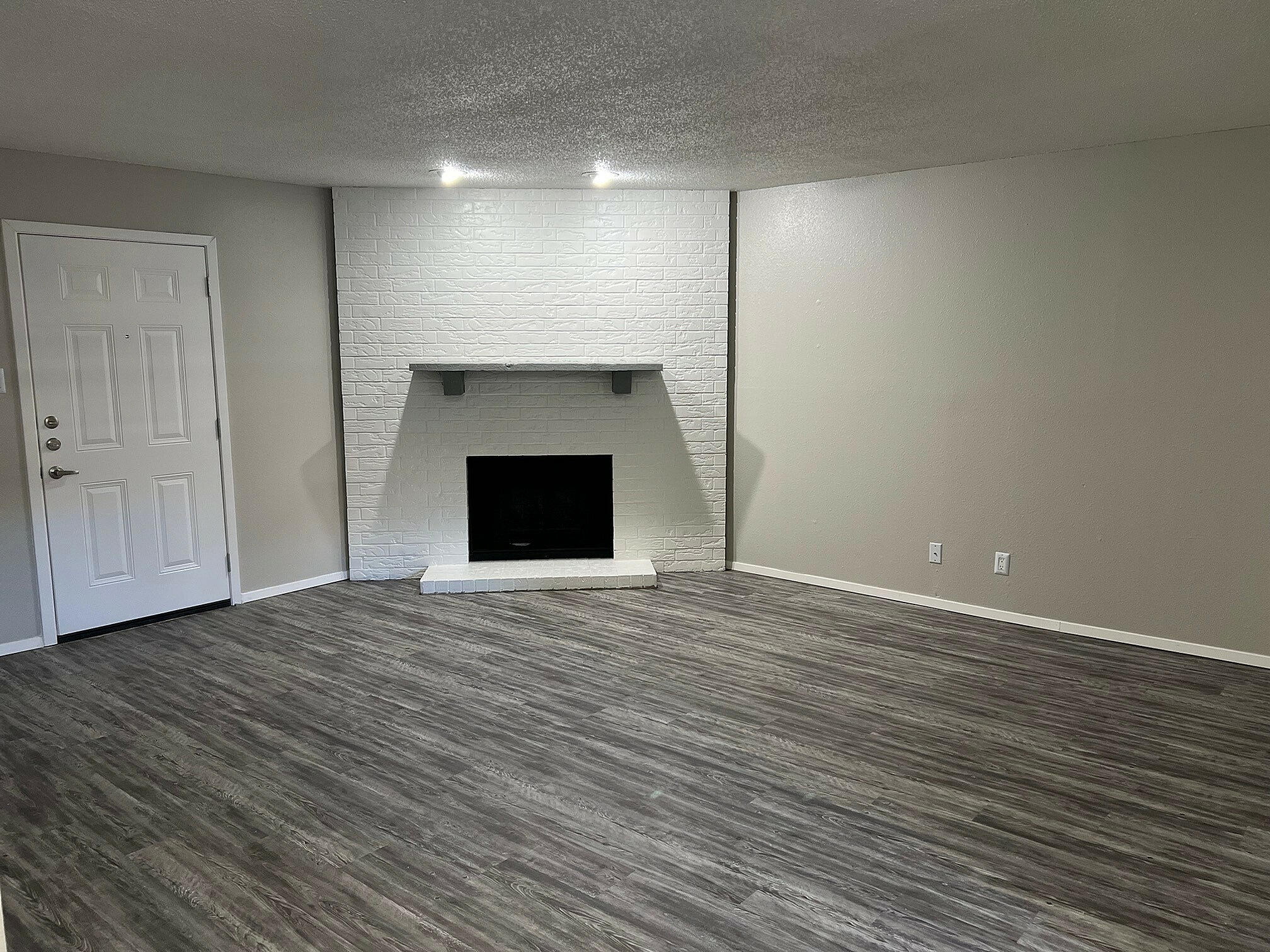 Spacious living room with modern vinyl plank flooring and a sleek white brick fireplace offering a welcoming ambiance.