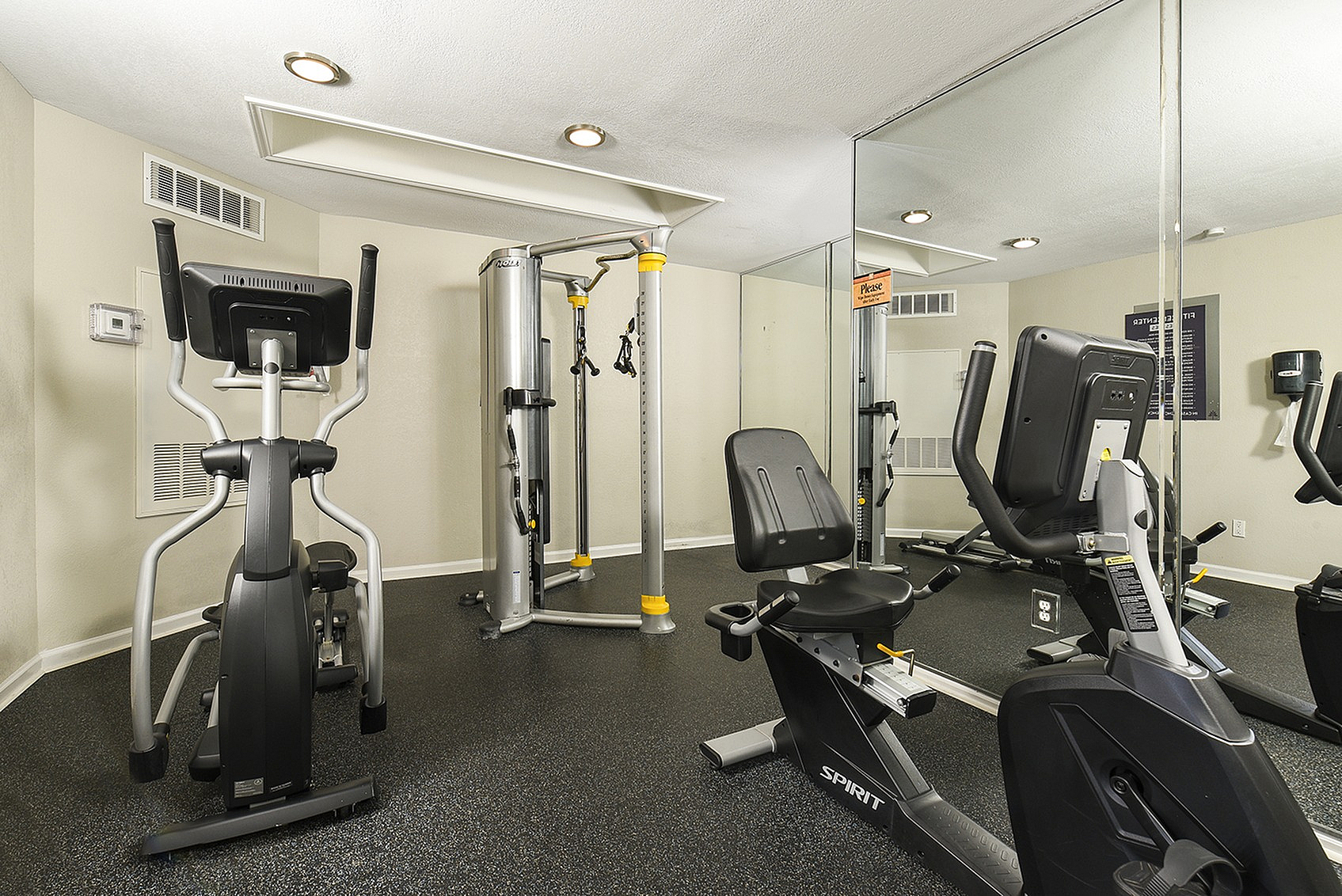 Modern fitness room featuring a sleek elliptical, multi-station gym equipment, and a stylish recumbent bike, ideal for a premium workout experience.