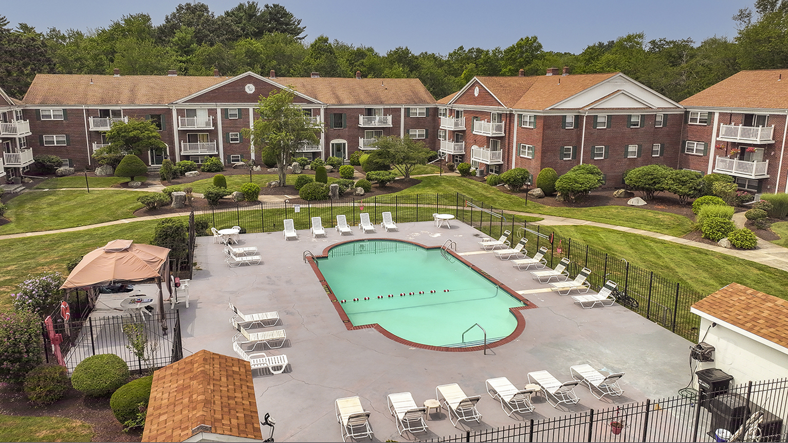 Lush apartment community with inviting swimming pool, surrounded by well-maintained gardens and elegant brick buildings.