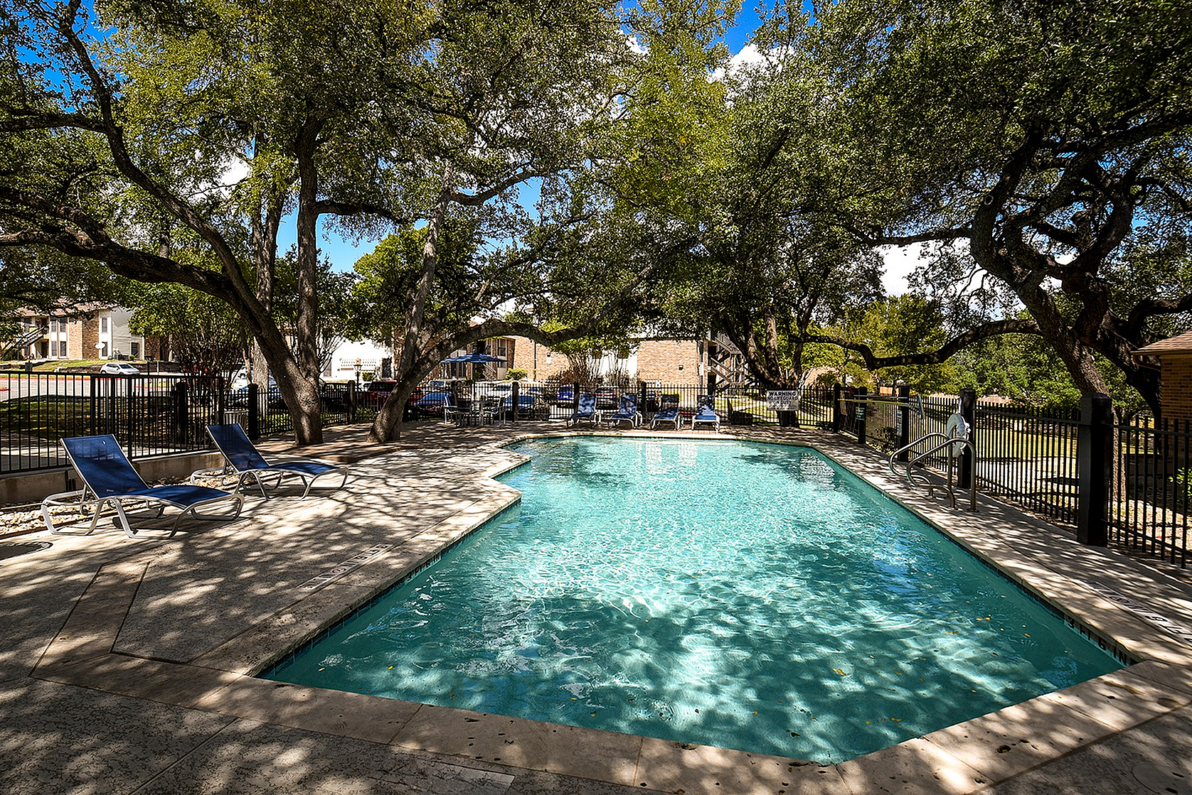 Inviting outdoor pool surrounded by lush trees and comfortable lounge chairs, offering a serene retreat within the apartment complex.