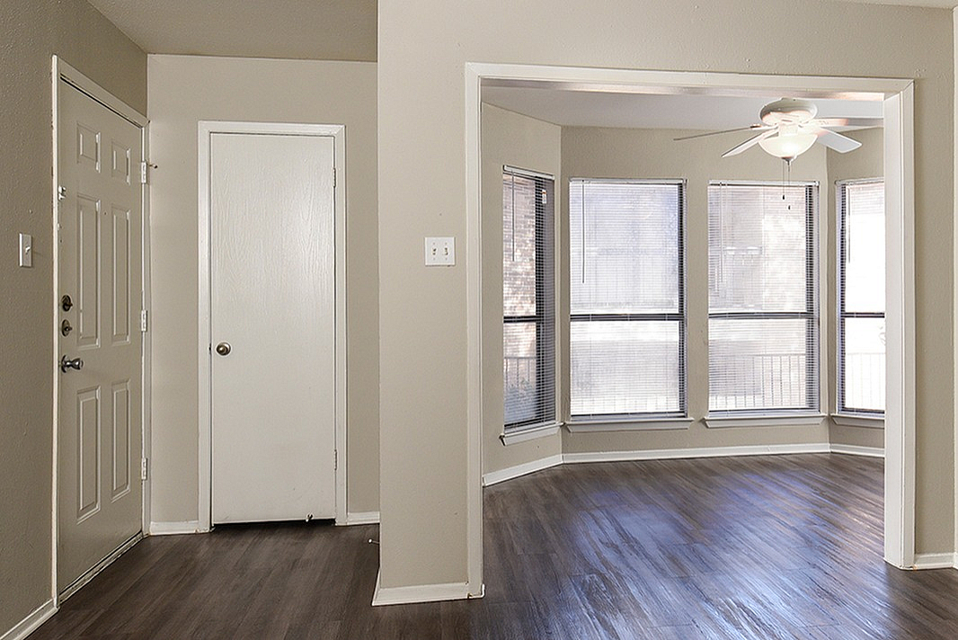 Bright apartment space featuring sleek vinyl flooring, modern ceiling fan, and large bay windows offering plenty of natural light.