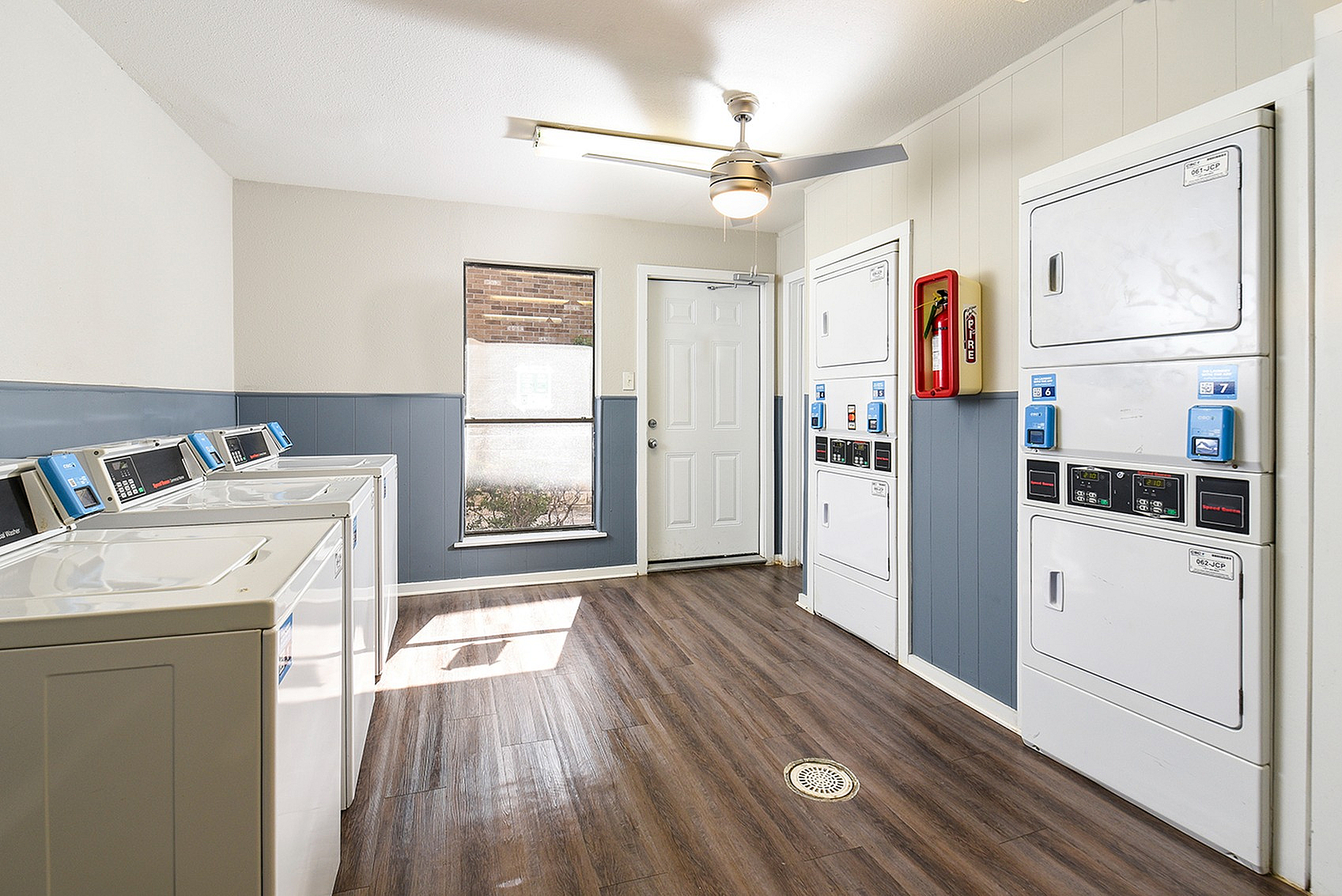 Bright and modern laundry room with stacked washers and dryers, sleek overhead lighting, and tasteful wood flooring.