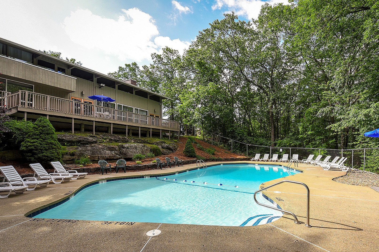 Inviting outdoor swimming pool surrounded by lush greenery and spacious sun deck with lounge chairs, perfect for relaxation.