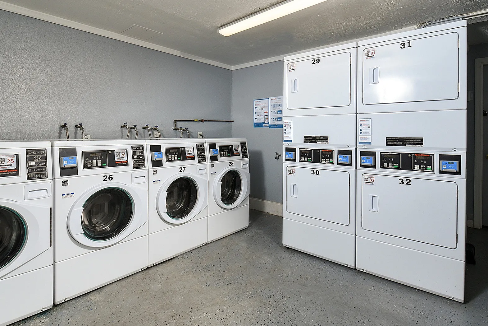 Bright and modern laundry room featuring multiple high-efficiency washers and dryers in a clean, accessible space.
