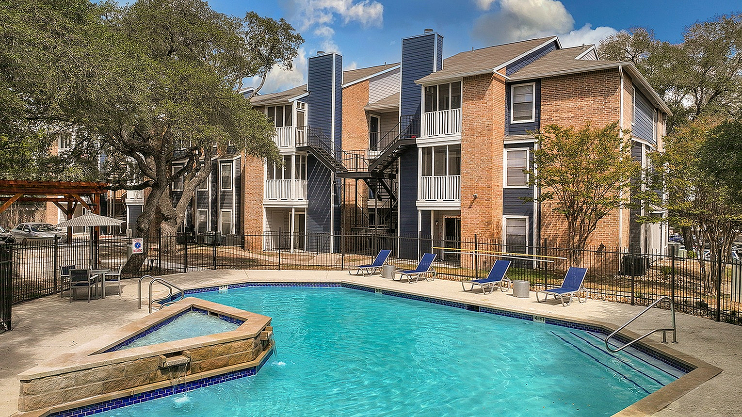 Inviting apartment complex with a sparkling blue pool, surrounded by modern brick buildings and lush greenery, perfect for relaxation and leisure.