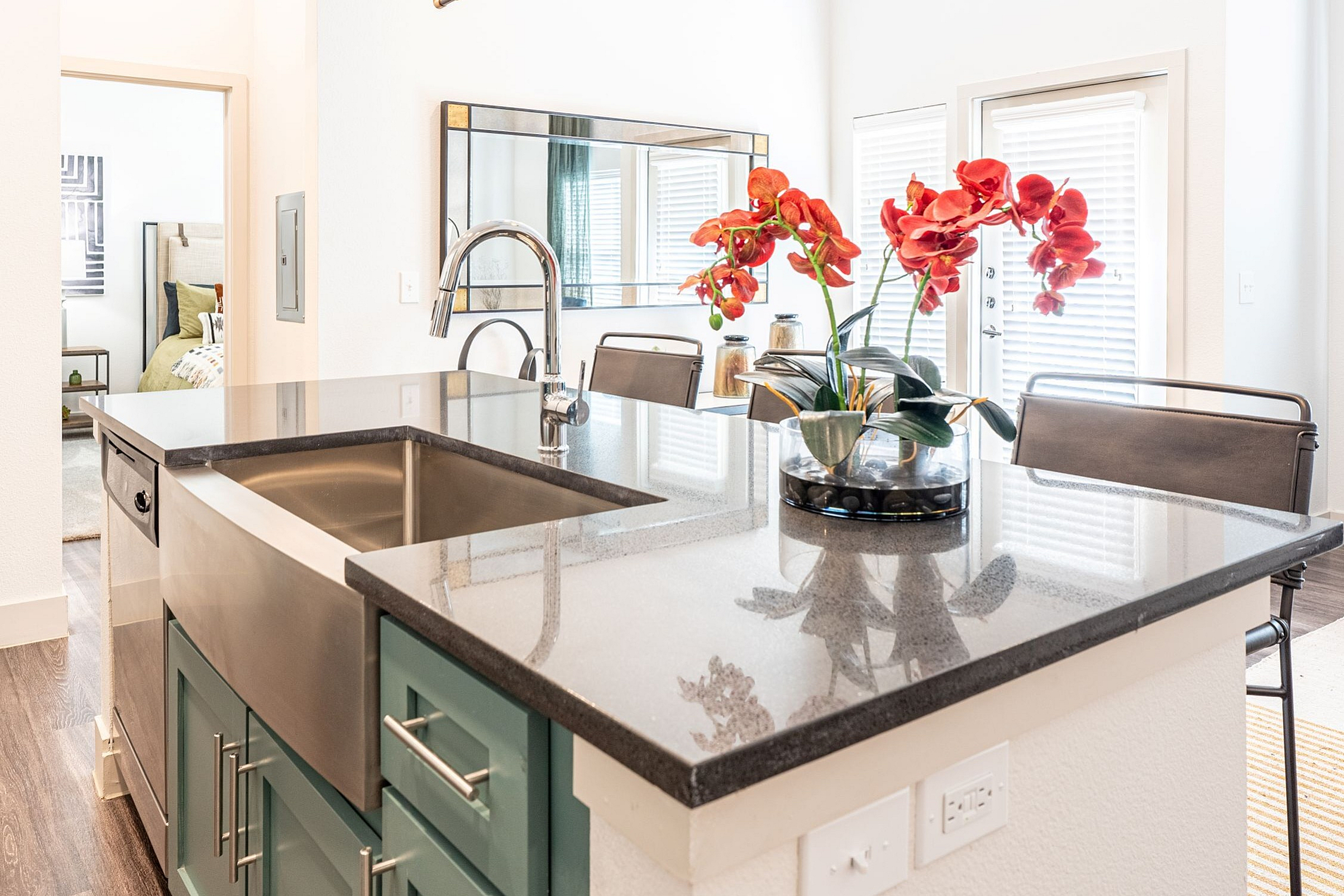 Modern kitchen with sleek granite countertops, stainless steel sink, and elegant pendant lighting, complemented by vibrant red orchids.