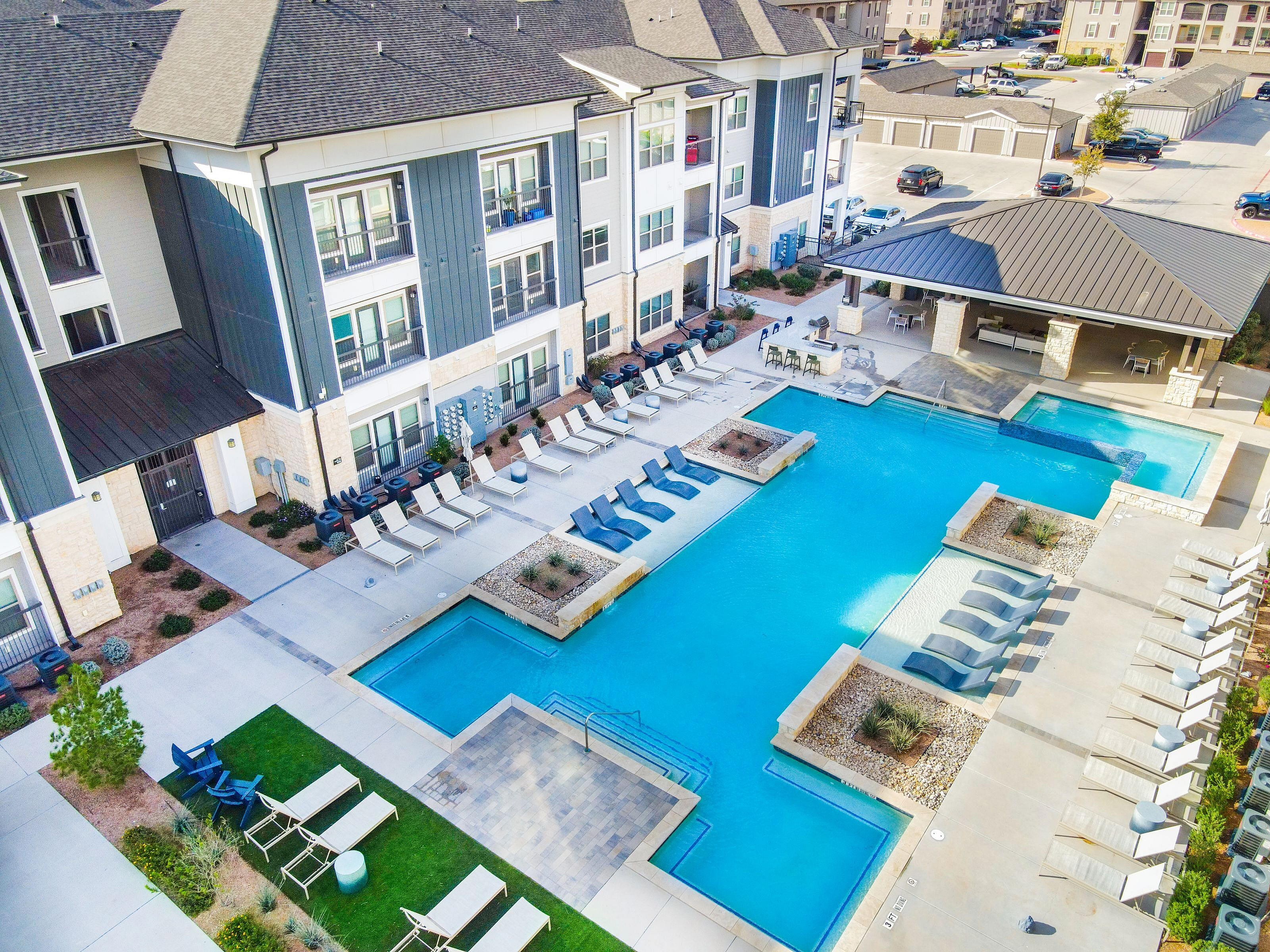 Luxurious apartment complex with a sparkling pool, stylish outdoor seating, and modern architectural design.