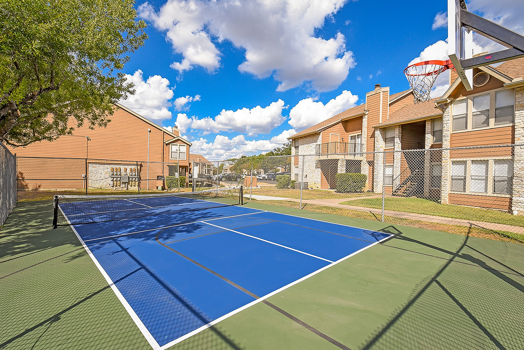 Charming apartment complex with a sunny, blue basketball and tennis court surrounded by lush greenery and stylish architecture.