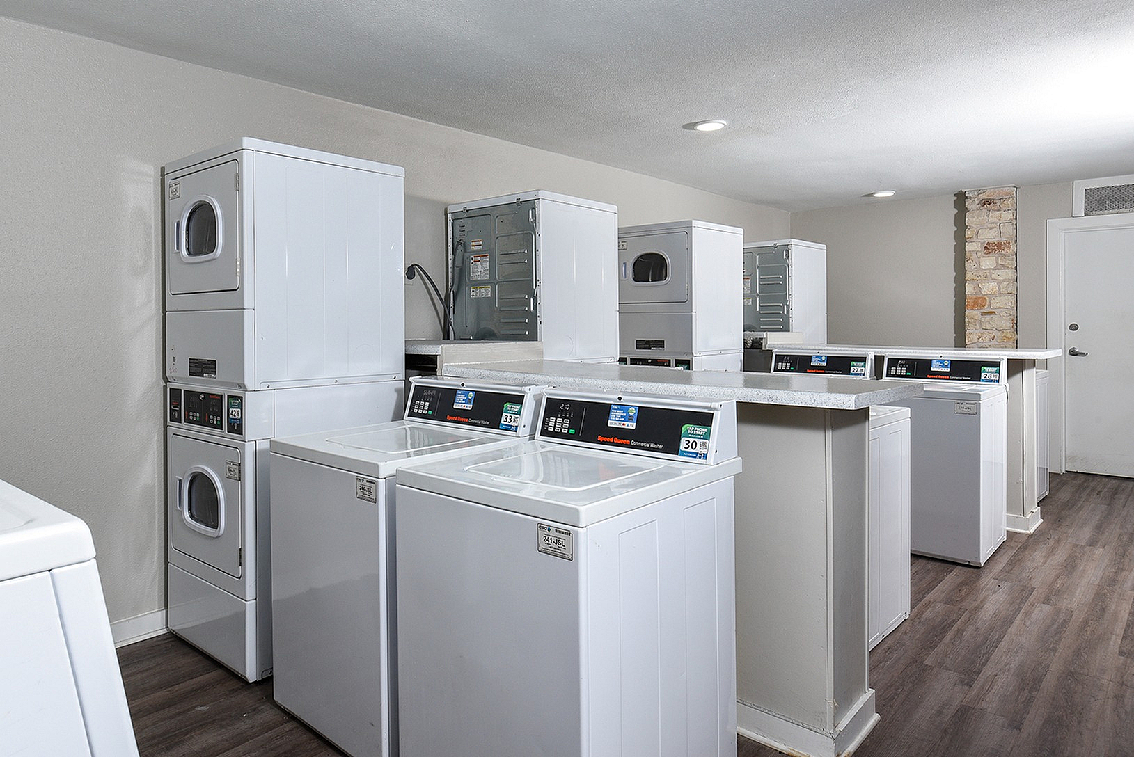 Modern communal laundry room with multiple white washing machines and dryers, featuring sleek countertops and dark wood flooring.