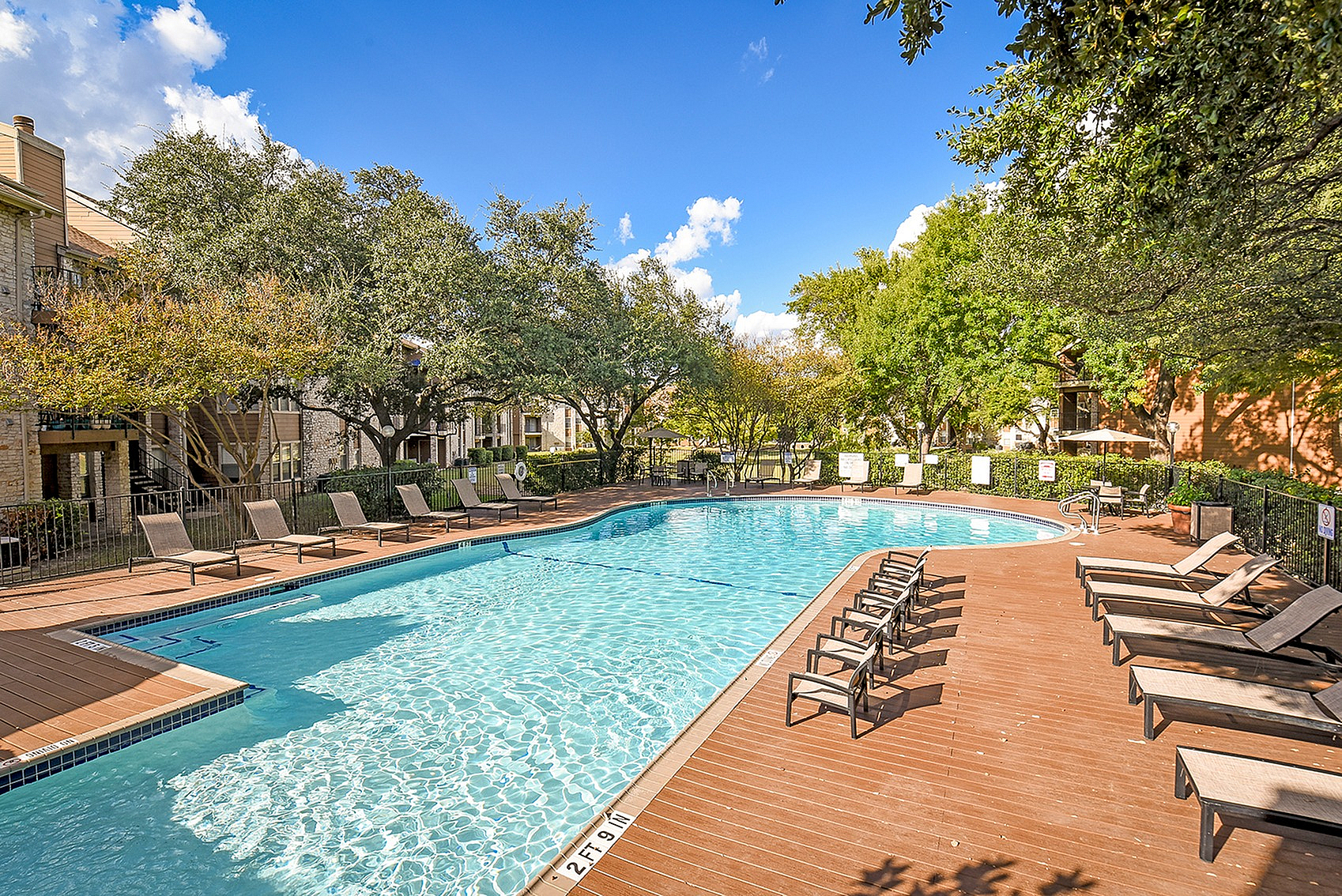 Inviting outdoor pool area with stylish lounge chairs, surrounded by lush green trees and modern apartment buildings.