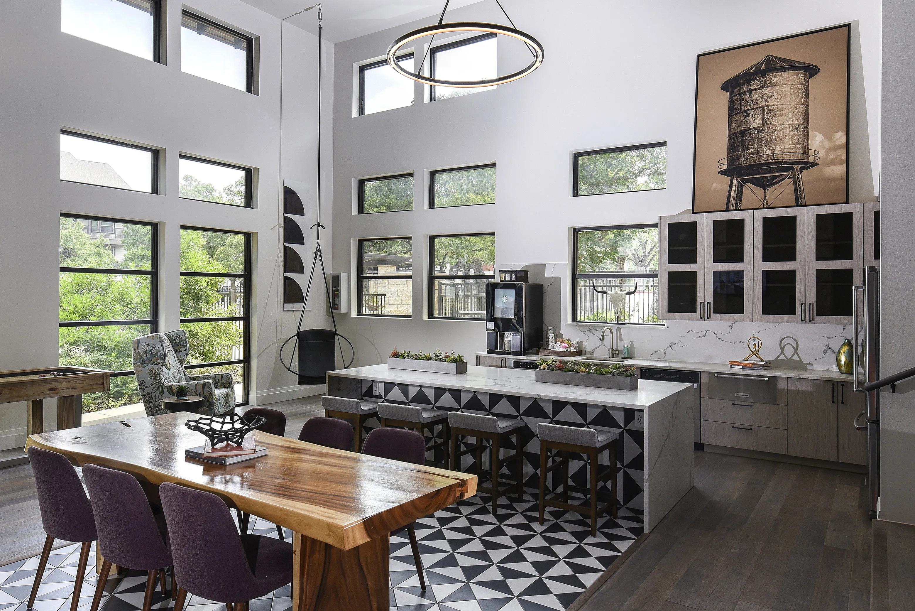 Modern kitchen with high ceilings, geometric tile floor, and a large natural wood dining table, enhanced by abundant natural light from multiple windows.