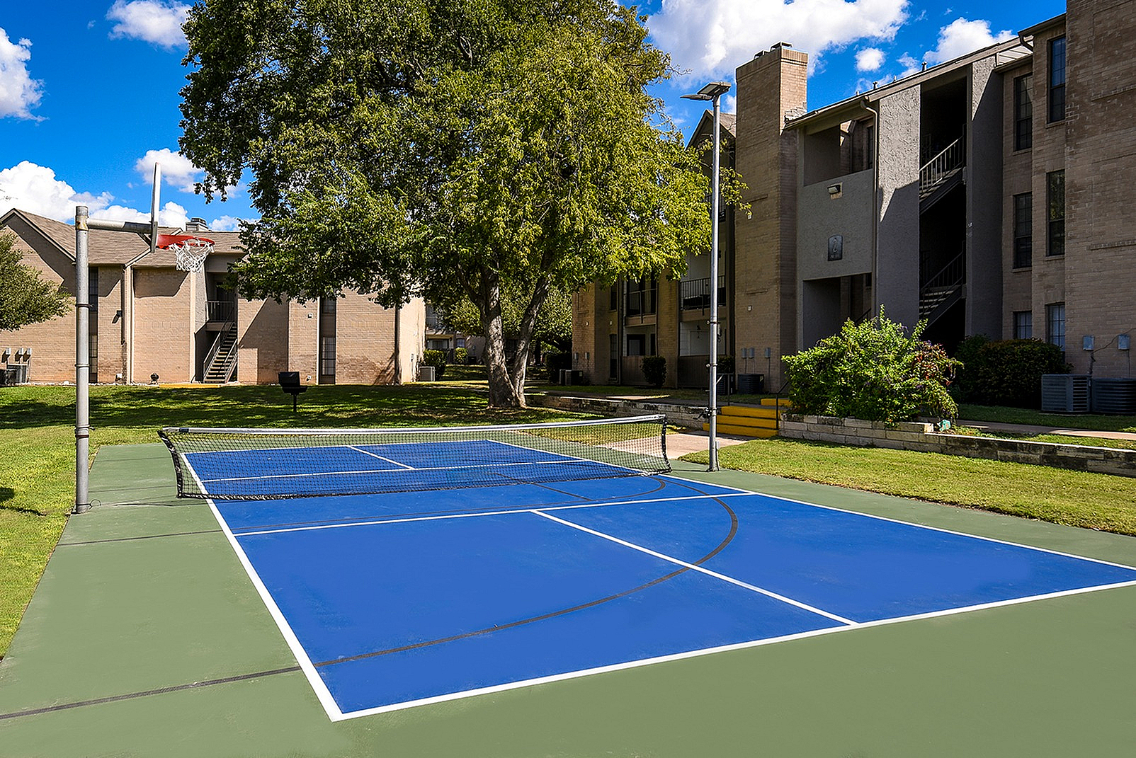 Charming apartment complex with vibrant outdoor basketball and tennis court nestled in lush greenery.