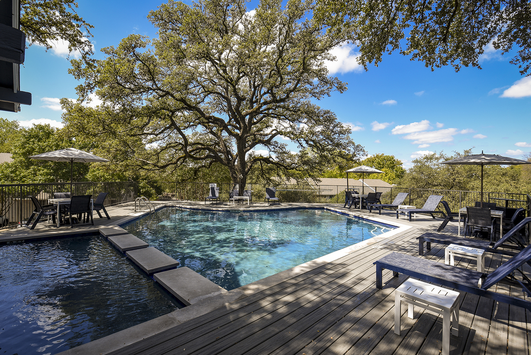 Serene outdoor pool with luxurious lounge chairs and umbrellas, surrounded by lush trees under a vibrant blue sky.