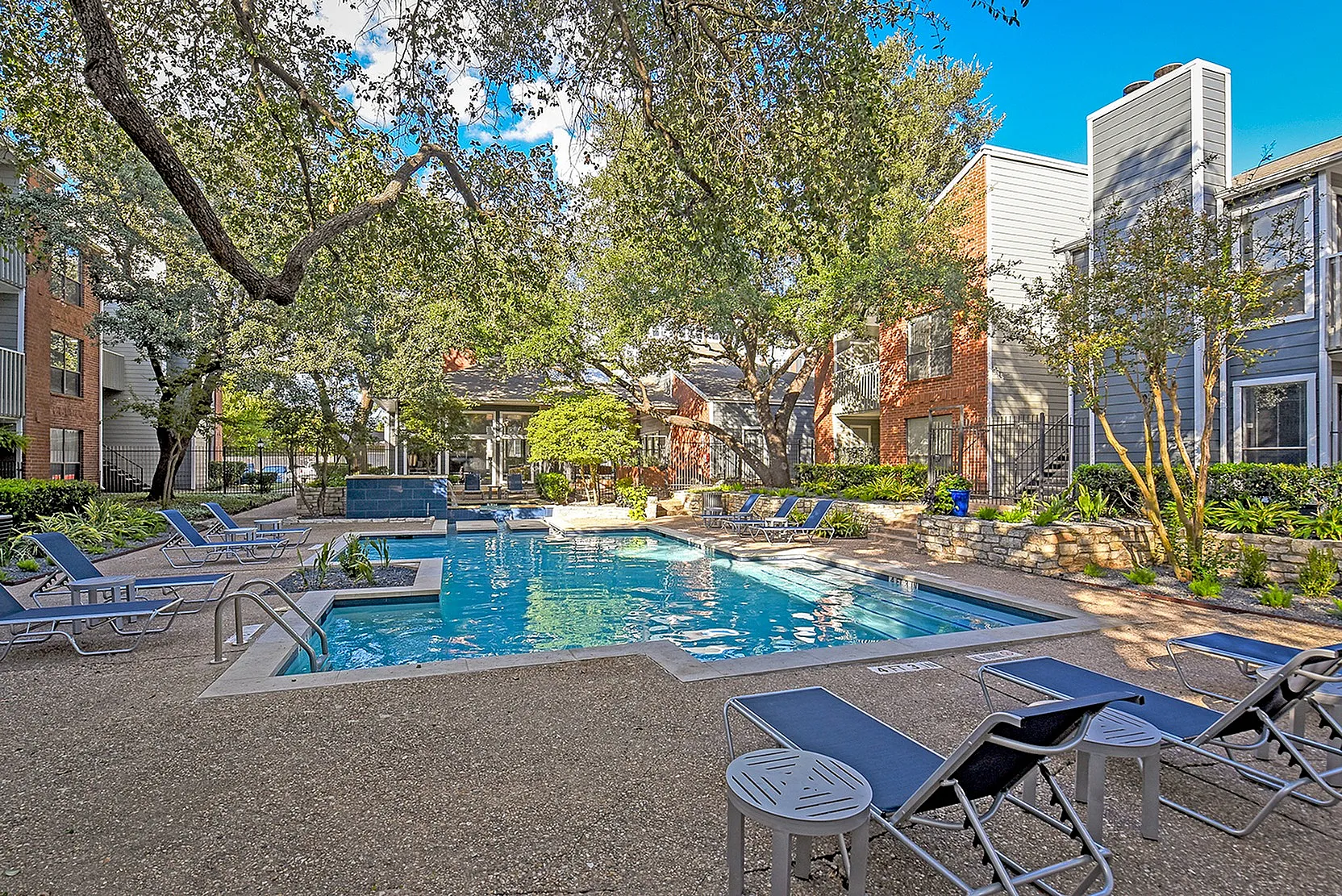 Inviting outdoor pool area surrounded by lush greenery and modern apartment buildings, offering a relaxing and scenic retreat.