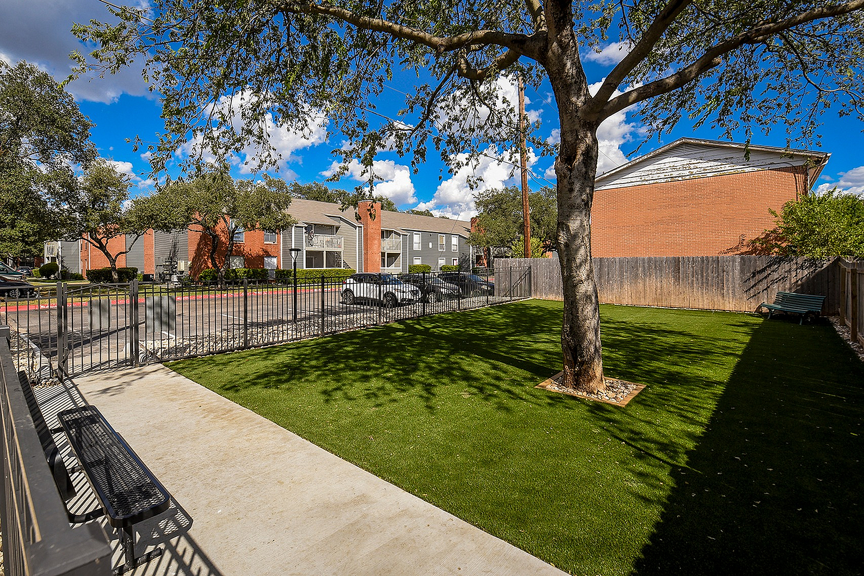 Inviting outdoor area with lush green lawn, shaded seating, and picturesque view of charming apartments, perfect for relaxation.