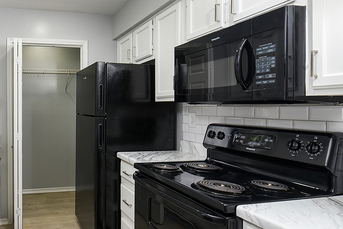 Modern kitchen with sleek black appliances, elegant white cabinetry, and polished marble countertops.