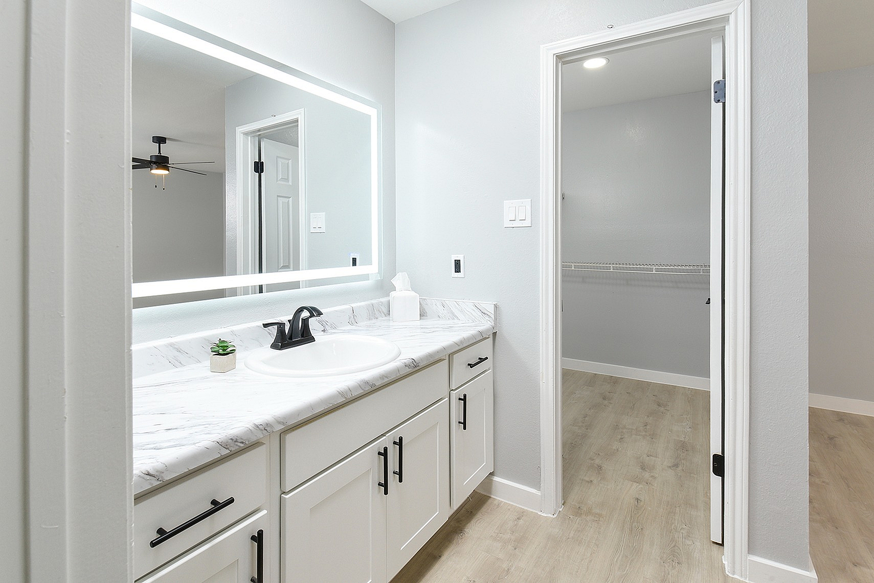 Elegant bathroom with a marble countertop, sleek black faucet, LED-lit mirror, and a spacious walk-in closet entrance.