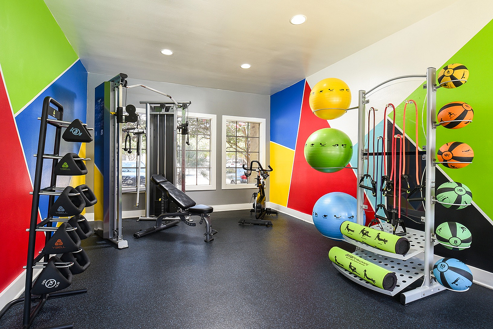 Vibrant gym room with colorful walls, featuring various exercise equipment including fitness balls, resistance bands, and modern workout machines.
