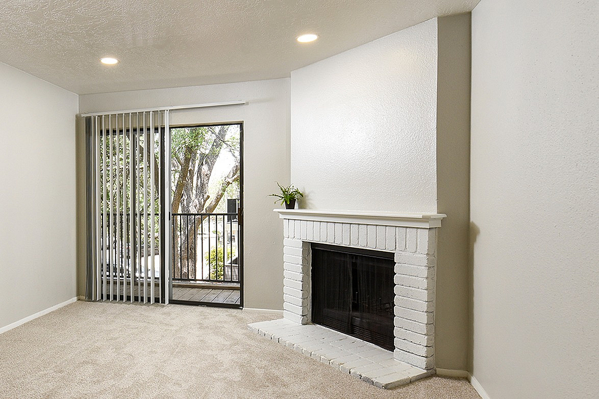 Bright living room with cozy fireplace, soft carpet, and large window leading to a balcony with a charming view.