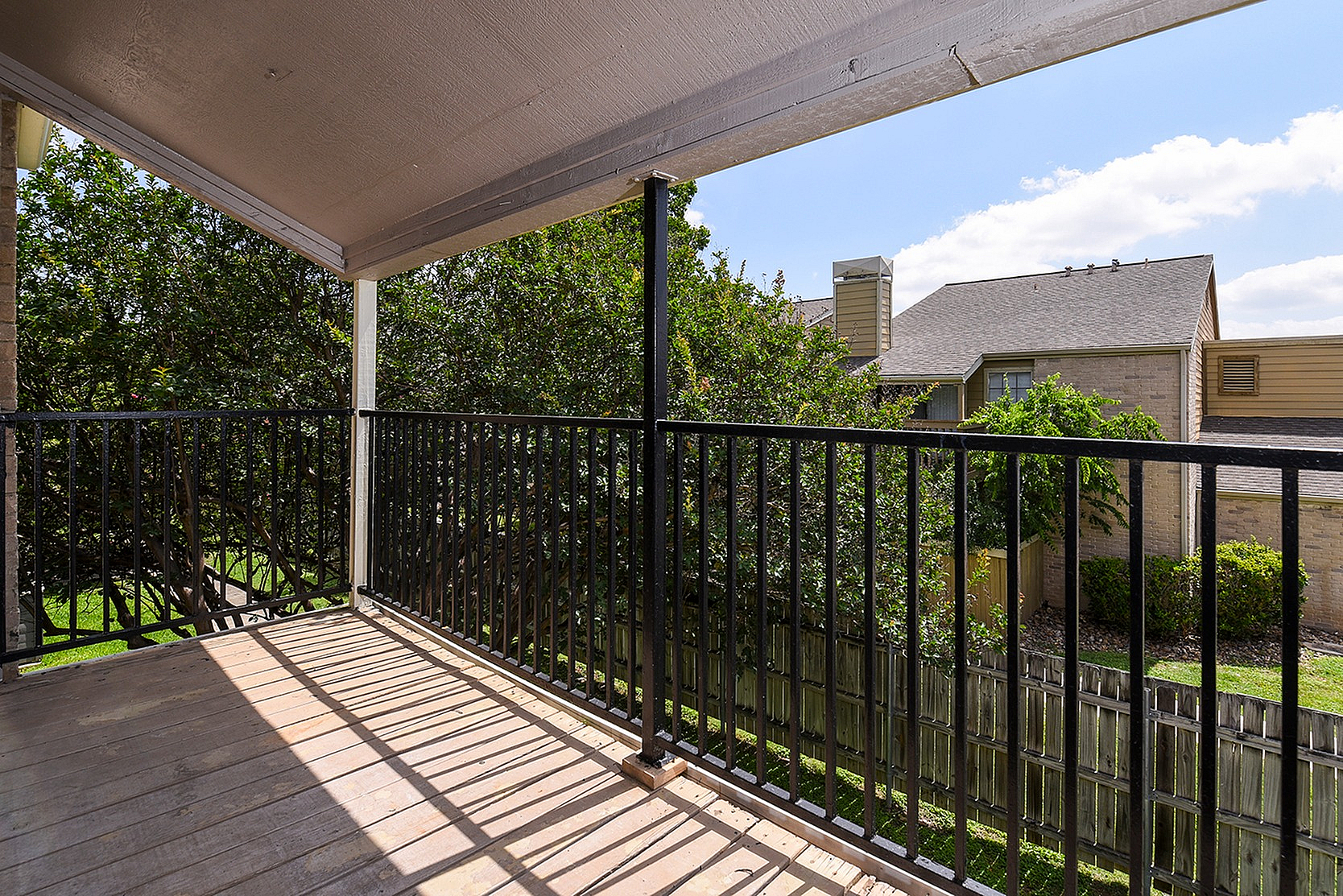 Inviting balcony with elegant railing, overlooking lush greenery and neighboring rooftops under a bright blue sky.