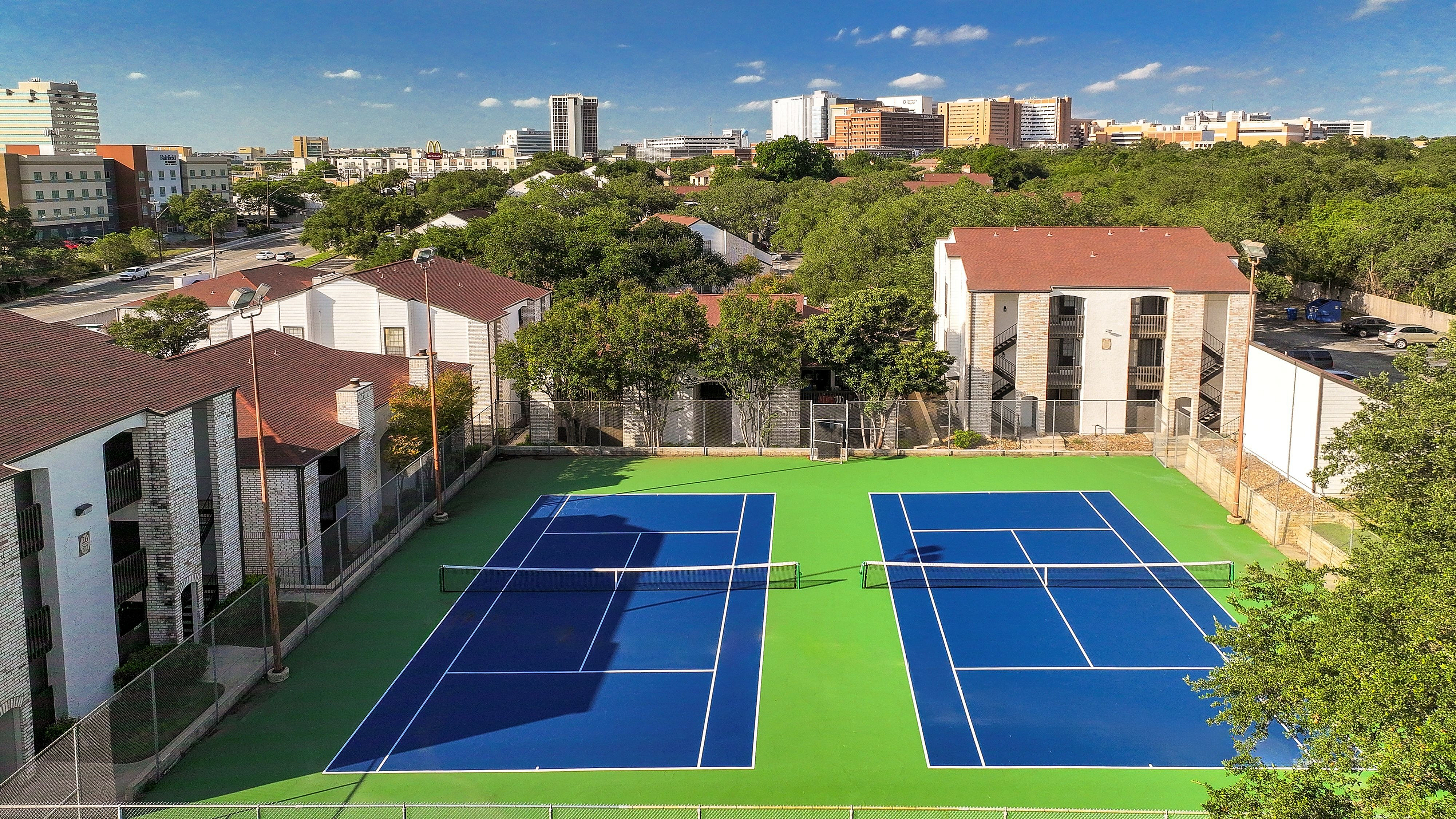 Vibrant tennis courts amidst lush greenery at a charming apartment complex, offering sunny views and recreation in the heart of the city.