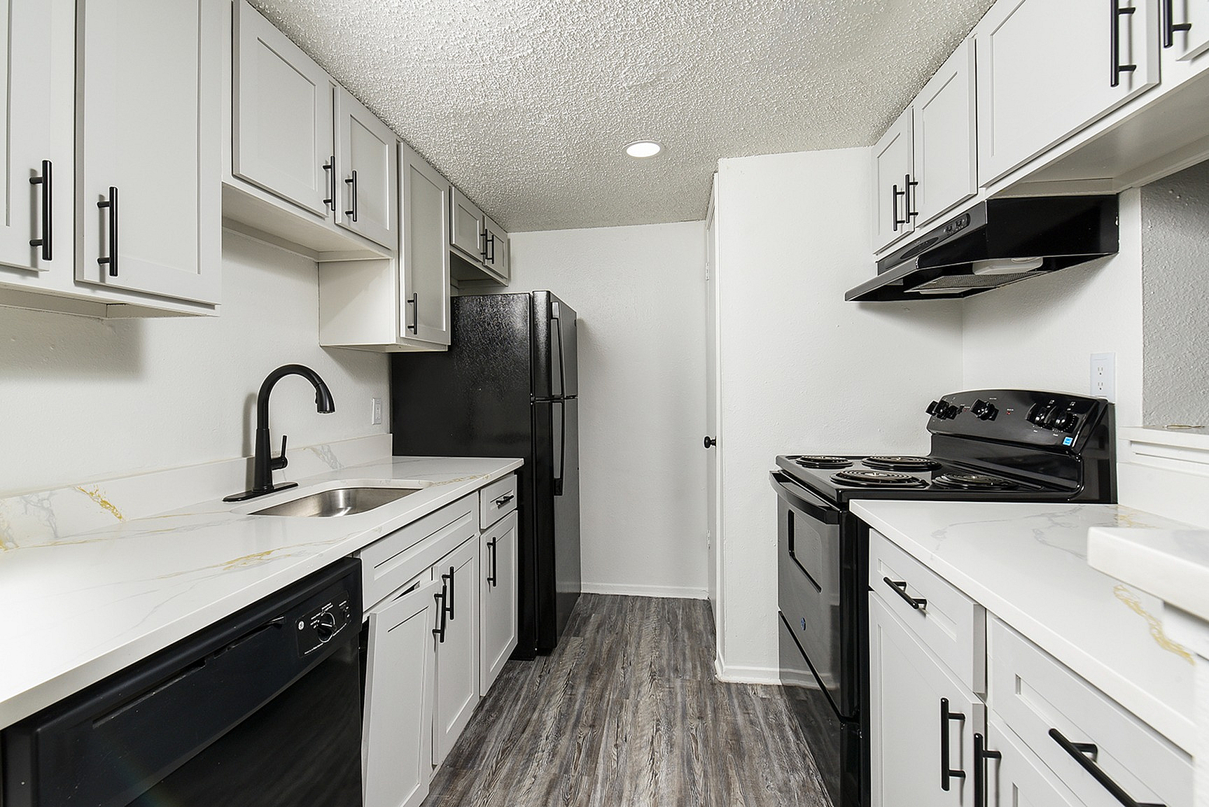 Sleek modern kitchen with elegant white cabinets, black appliances, and glossy countertops in a spacious layout.