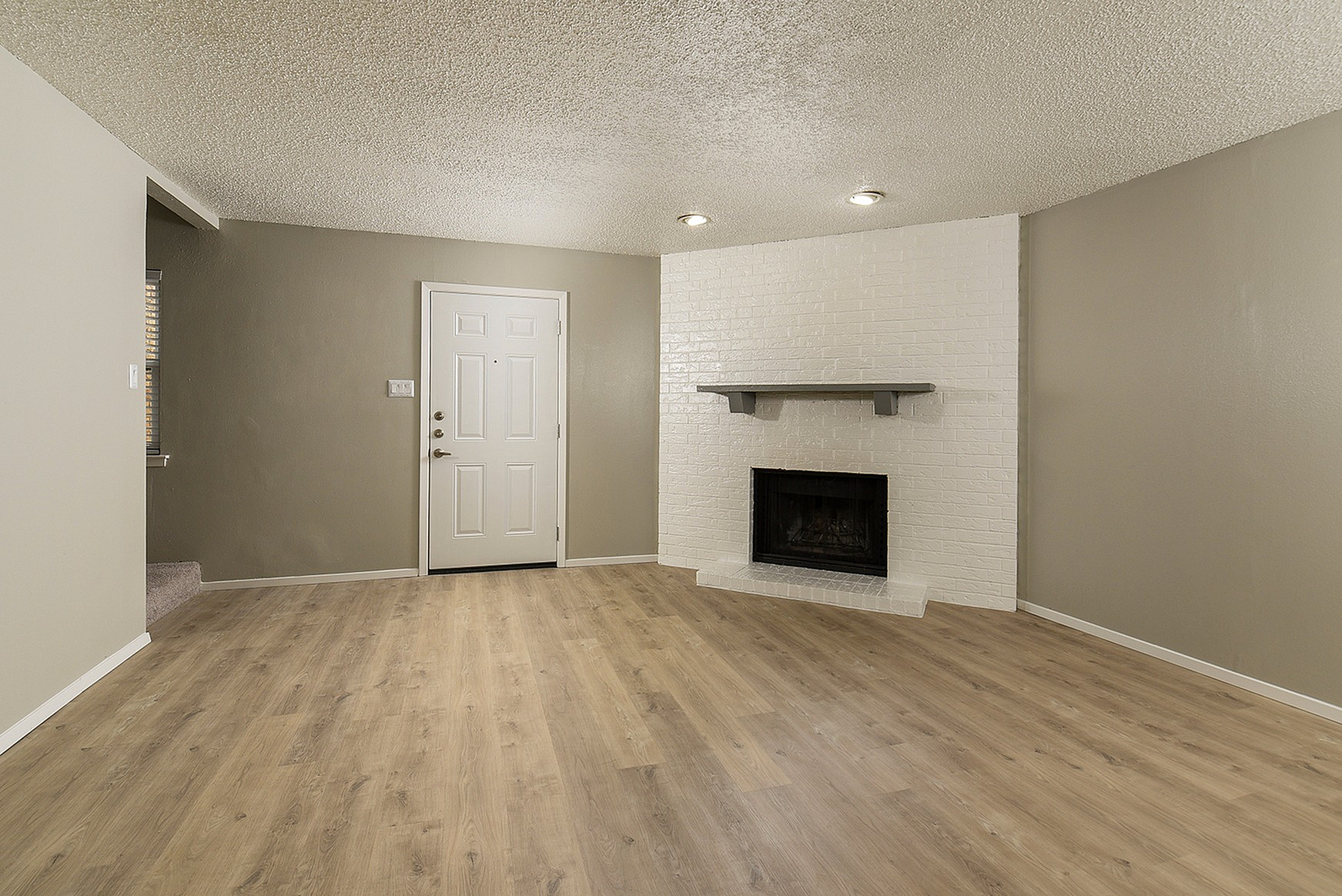 Inviting living room with elegant wood flooring, a charming white brick fireplace, and modern recessed lighting.