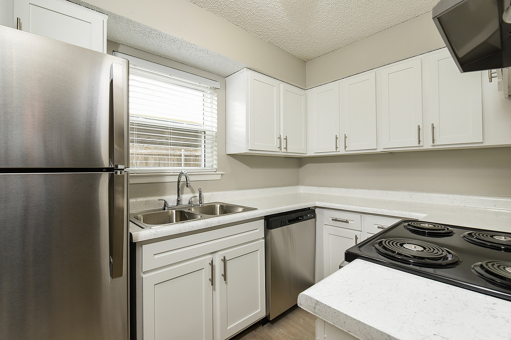 Modern kitchen featuring sleek stainless steel appliances, elegant white cabinetry, and a pristine double sink under a bright window.
